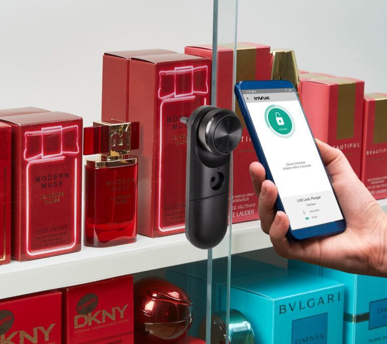 LIVE Plunger Lock on a glass door securing fragrance boxes with a hand holding a mobile phone