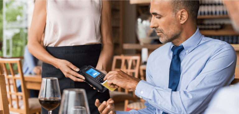 Homme utilisant un boîtier portable mPOS pour effectuer un paiement dans un restaurant.
